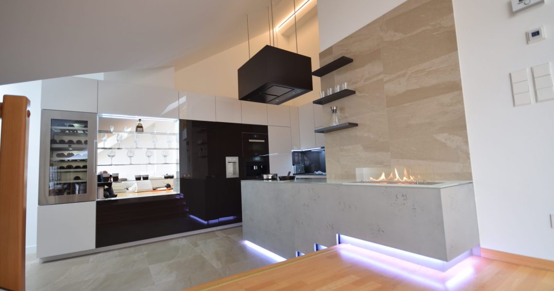 Offene Designküche mit Hochglanzfronten, Kochinsel in Betonoptik und integriertem Kamin