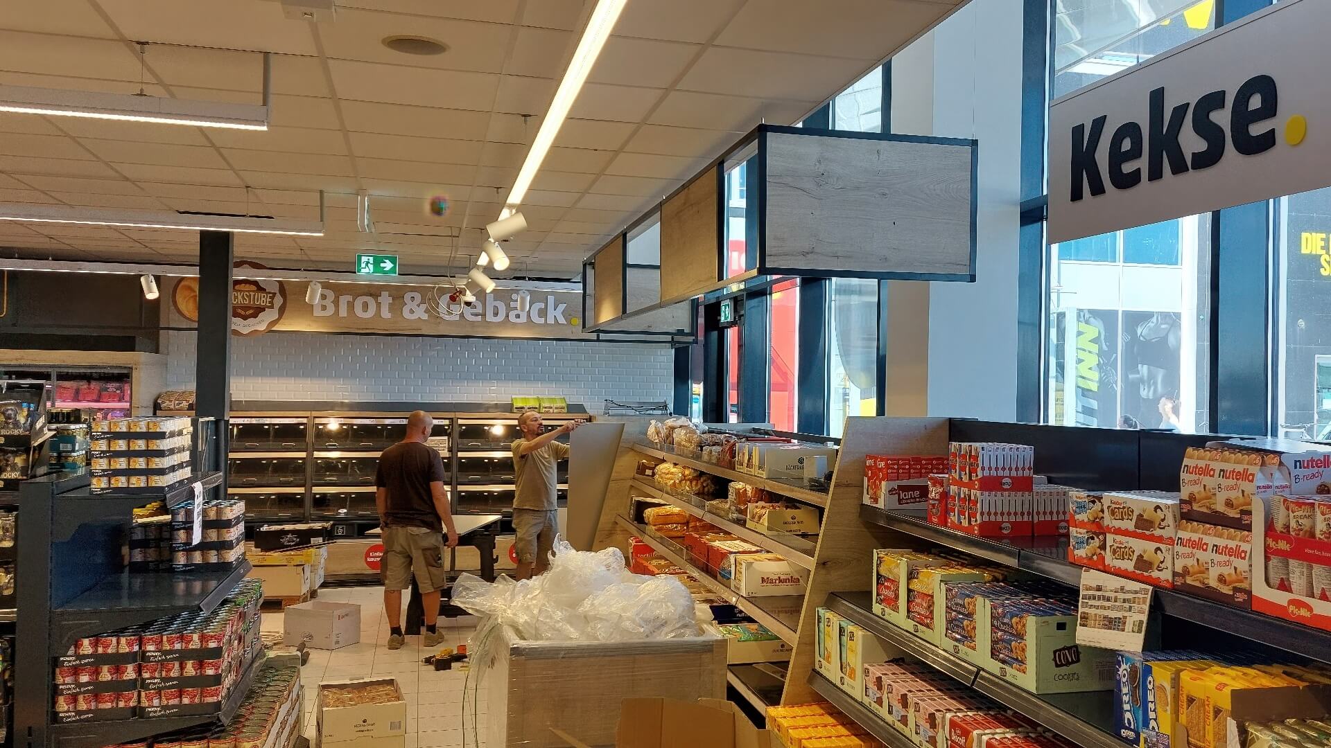 Marktbereich mit Regalen, Deckenschildern und Wandverkleidungen