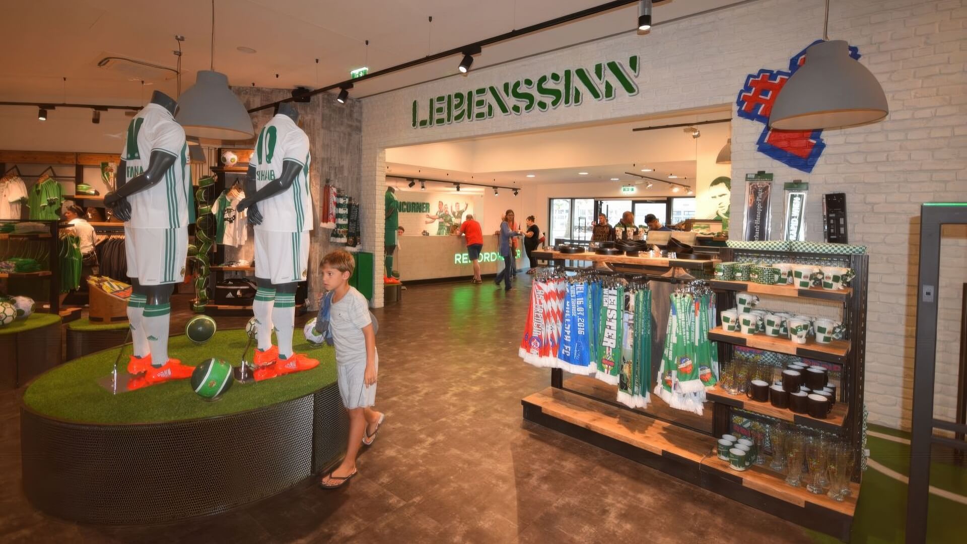 Fanshop mit grün-weißer Präsentationsfläche, Podeste mit Kunstrasen und Regalen