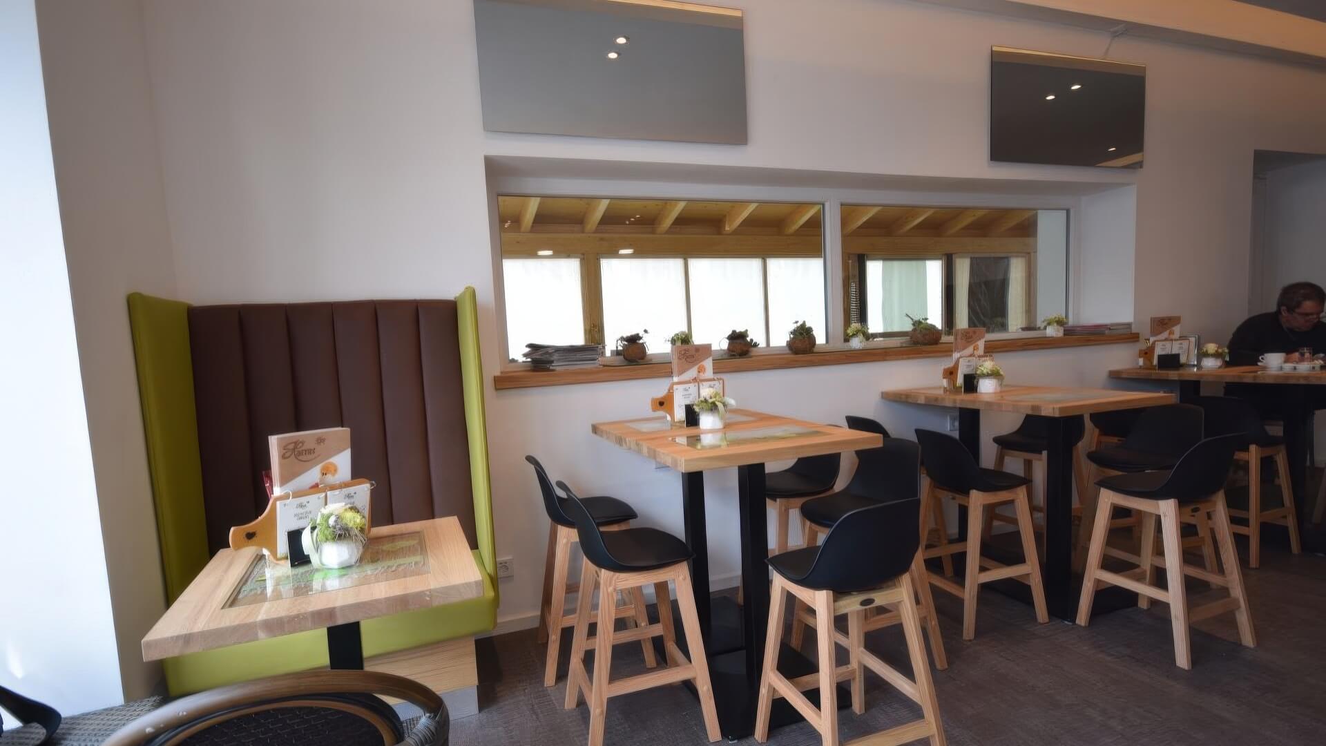 Massivholz-Bank mit tapezierter Rückenlehne, Eichen-Tisch und schwarze Barhocker im Eissalon