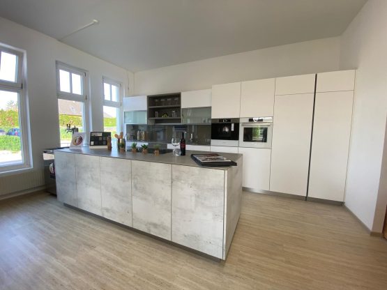 Moderne Einbauküche mit Kochinsel in Betonoptik und hochgebauten Geräten