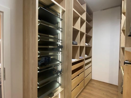 Offene Ankleide mit Holzregalen und beleuchtetem Schuhauszug