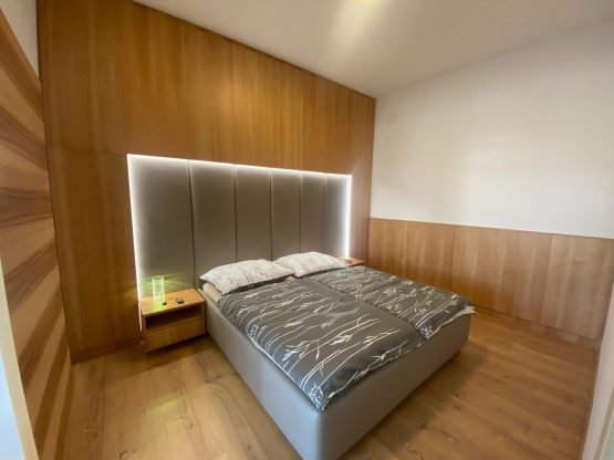 Schlafzimmer mit hinterleuchtetem Polsterbett und wandhoher Holzverkleidung