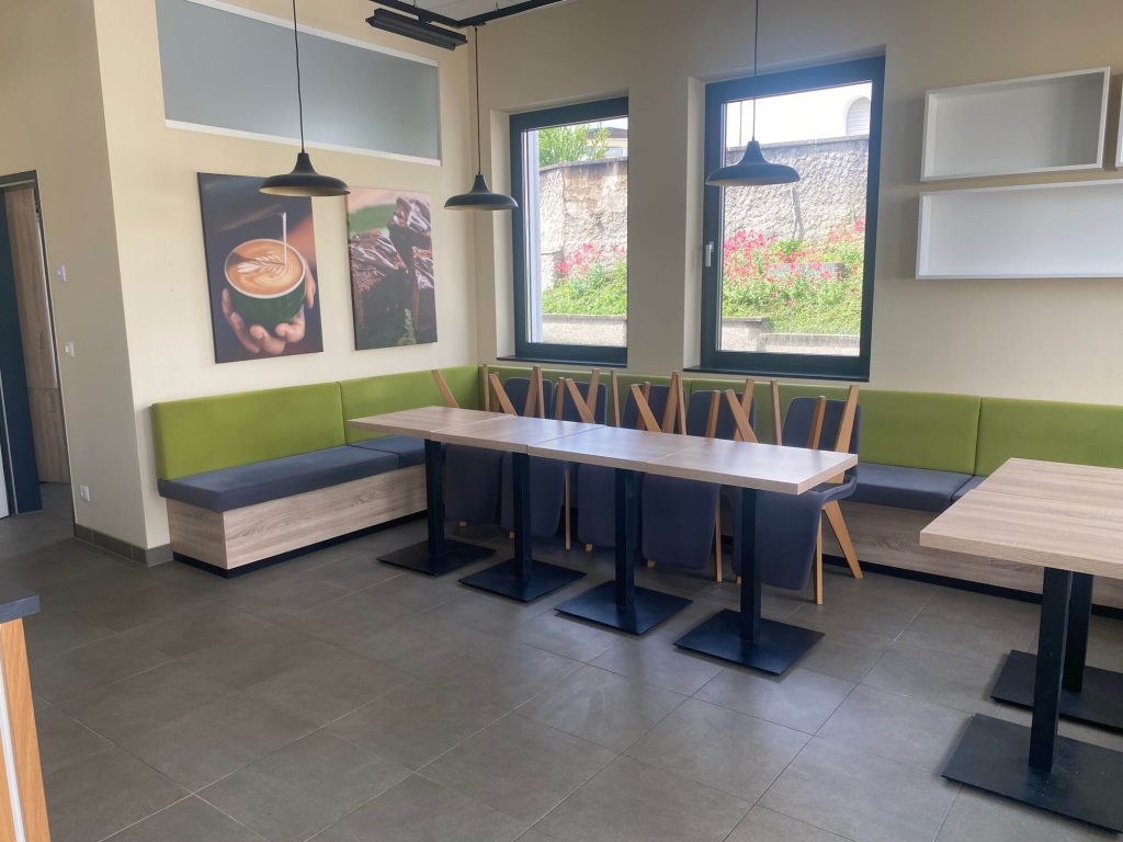 Moderner Sitzbereich mit langer Sitzbank, stilvollen Stühlen und Wandbildern im Café.